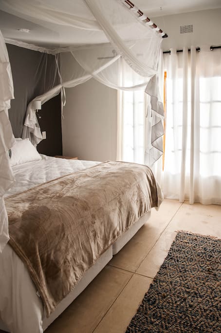 a bright and sun-lit air-conditioned bedroom boasting crisp white linen and 5-star quality bed