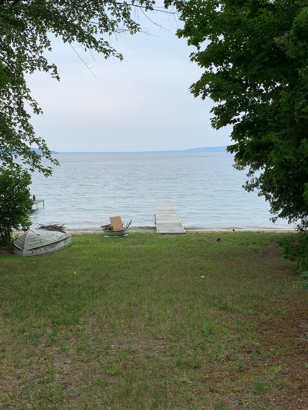 A serene view of Crystal Lake is presented, featuring a wooden dock extending into the water. Lush greenery frames the scene, while a small grassy area leads to the lakeshore. An old boat and a beach chair are positioned nearby, enhancing the tranquil setting.
