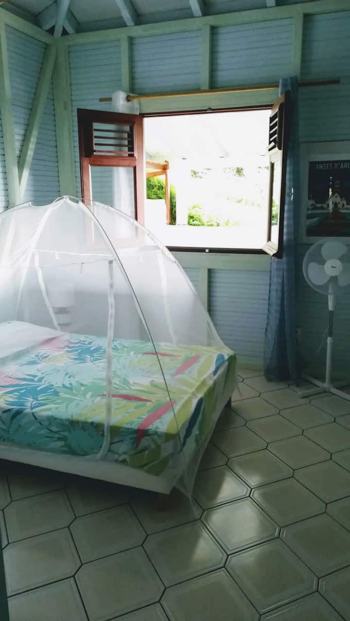 Blue room with hanging space, fan, mosquito net, and sea view.