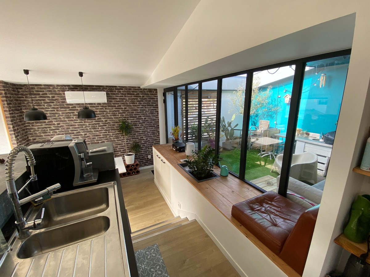 A well-appointed kitchen area features sleek appliances against a backdrop of exposed brick. Large windows illuminate the space, offering views of an outdoor terrace, while a cozy seating nook is positioned by the window, enhancing the connection between indoor and outdoor areas.