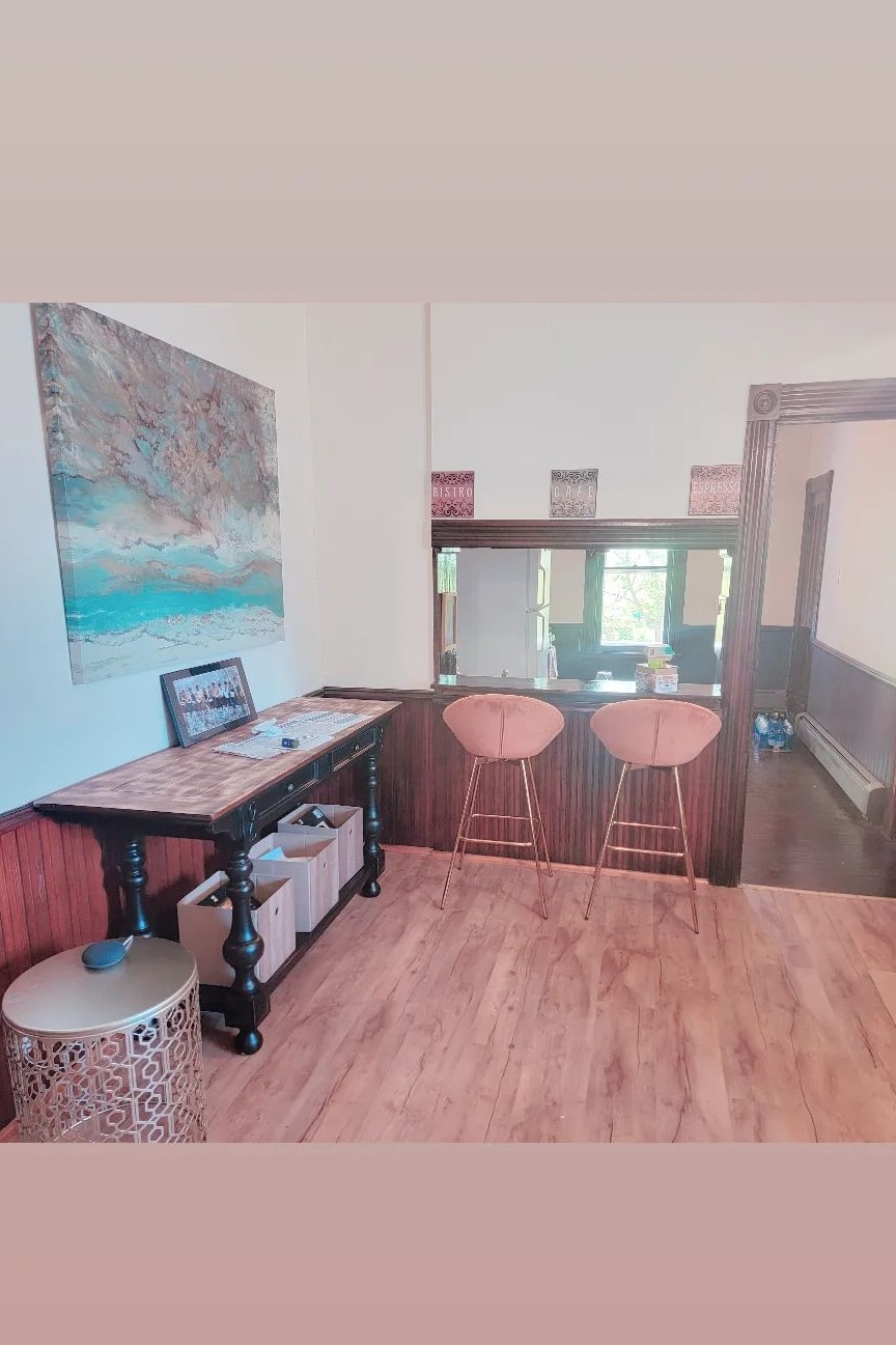 A small entryway features two bar stools positioned at a stylish console table. A large piece of art hangs on the wall, reflecting shades of blue and brown. Natural light filters in, creating a welcoming atmosphere throughout the space.