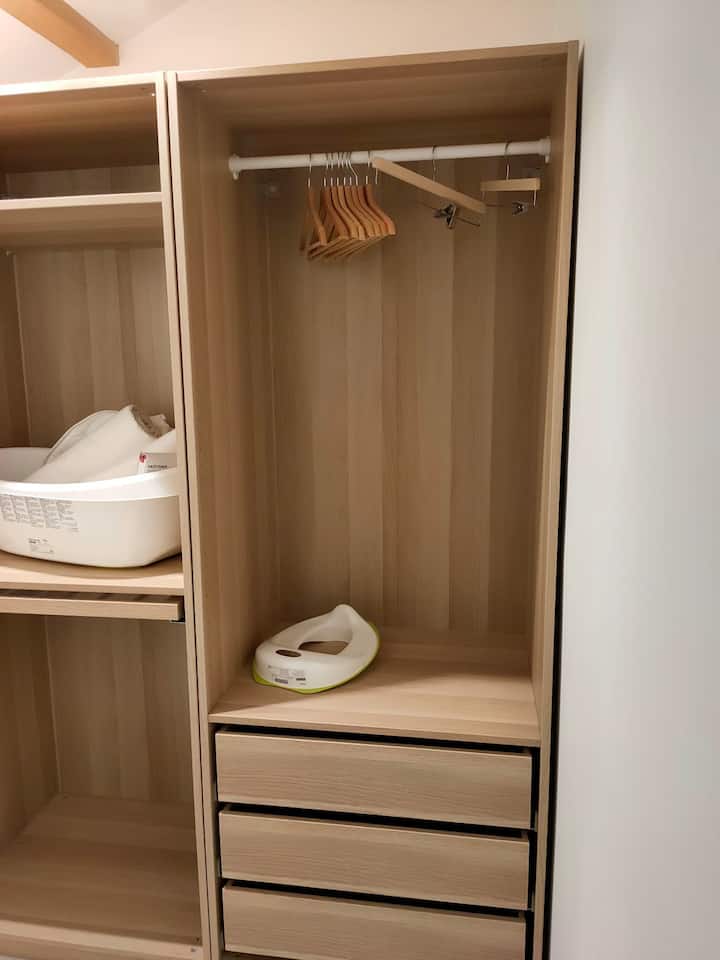 Vstavaný šatník s príslušenstvom pre malé deti. Poloha detskej postieľky naľavo, čo vytvára malé oddelenie od hlavnej spálne, ktorá je za fotografom so sprchovacím kútom.