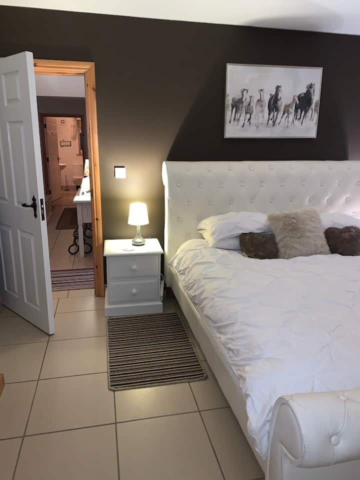 Მთავარი საძინებელი დიდი ზომის საწოლით, რომელიც დერეფნისკენ მიდის