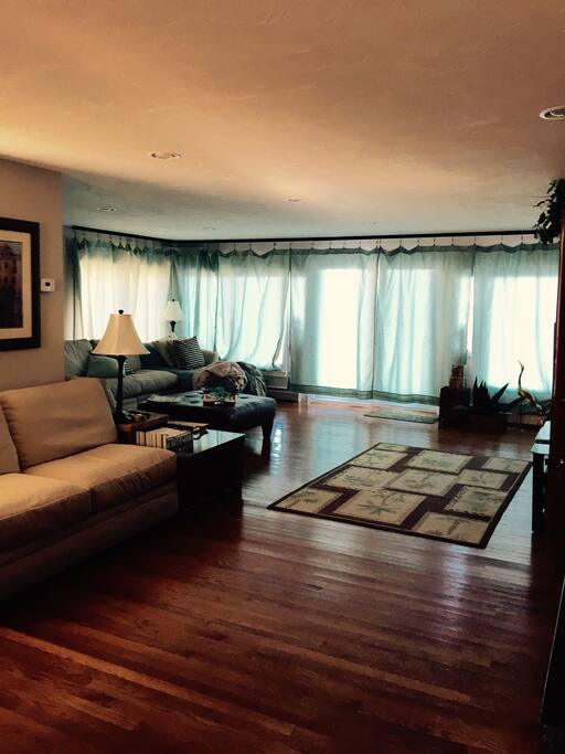 Living room view with wrap around sectional seating for 12 people, gas fireplace, oak flooring, area rug, 4 large Anderson window sliders that open to back deck facing Billington Sea, 55" screen Flat Panel TV.
