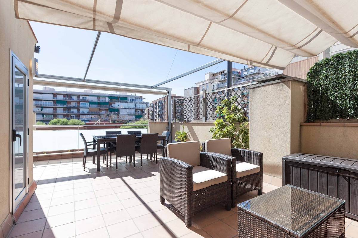 A spacious private terrace is presented, featuring comfortable seating and a dining area. Two shaded lounge chairs and a table are arranged on tiled flooring, surrounded by greenery. The terrace overlooks a tranquil courtyard, benefiting from bright natural light.