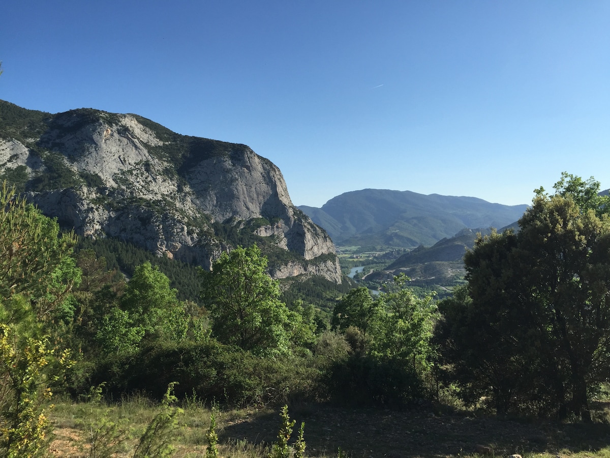 A scenic view of rugged mountains stands under a clear blue sky, with lush greenery in the foreground. Rolling hills and valleys are visible in the distance, creating a serene natural landscape, indicative of the surrounding terrain near the apartment.