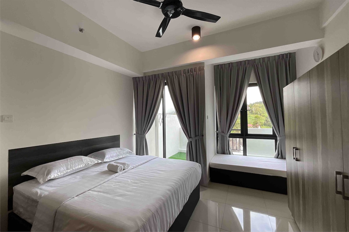 A well-lit sleeping area features a spacious bed with crisp linens, complemented by soft gray curtains. Natural light enters through a large window, illuminating a minimalist design that includes a cozy seating area beside it.