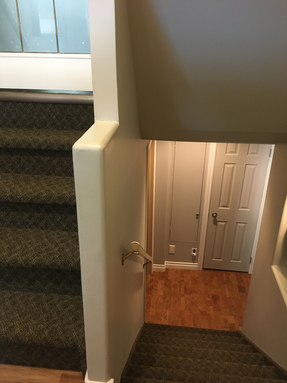 A view of the staircase leads to a well-lit hallway with a door at the end. The carpeted steps and a handrail are visible, while the walls are painted in neutral tones. A light illuminates the entrance, creating a welcoming transition between levels.