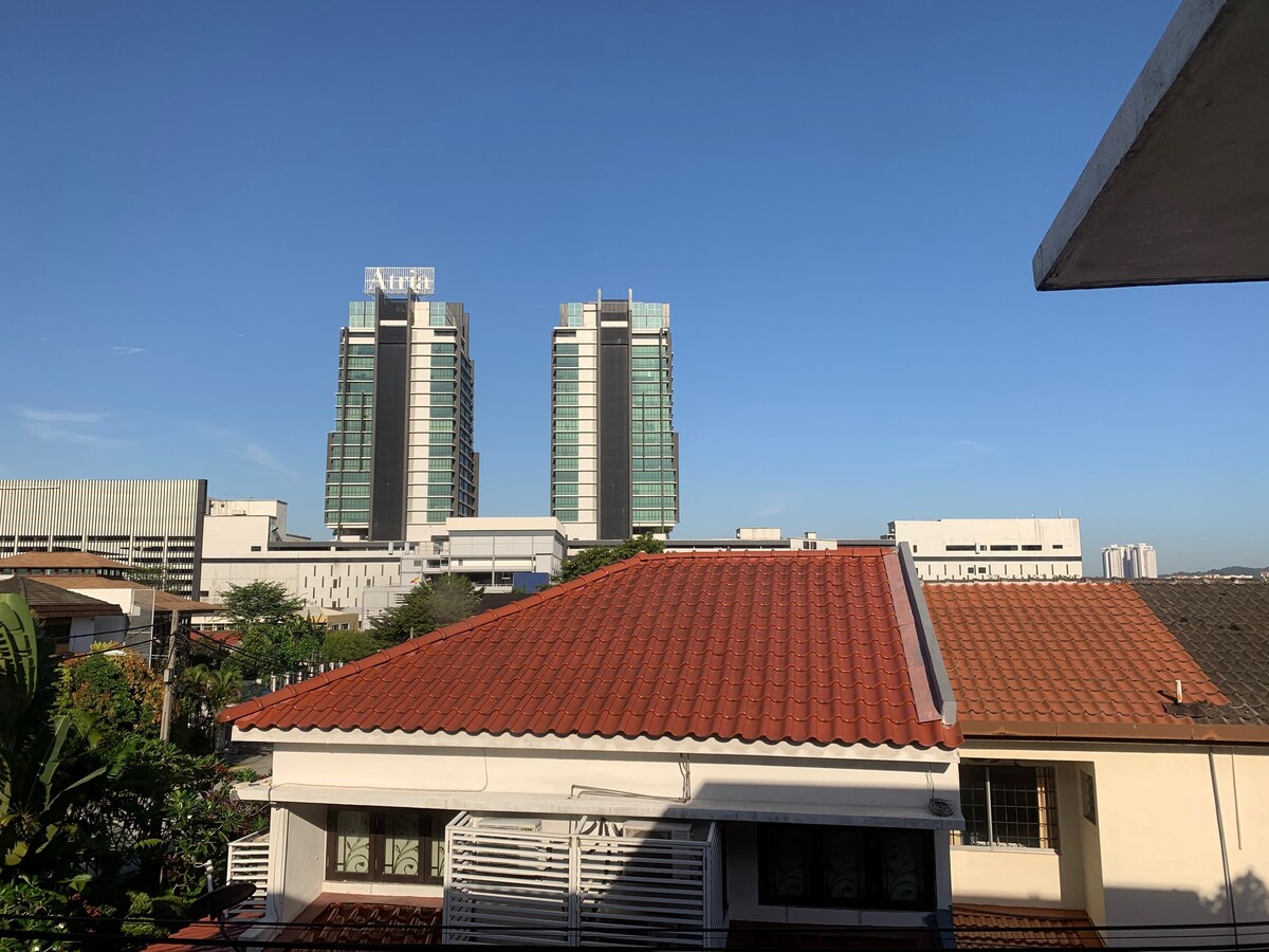 The image captures a clear view of modern high-rise buildings in the distance, including the Atria shopping complex. The foreground reveals traditional rooftops, providing a contrast to the contemporary architecture. A bright blue sky enhances the ambience of the scene.