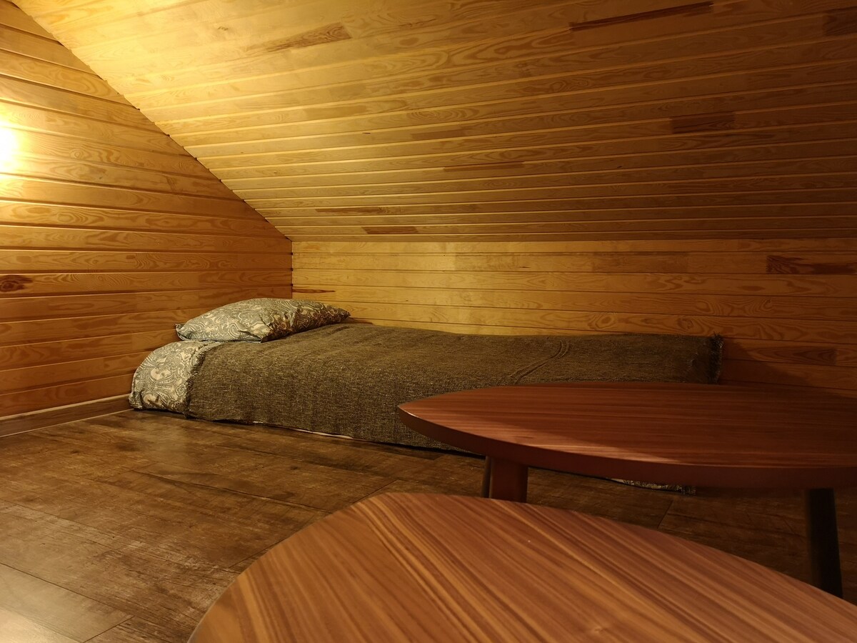 חדר על הגג עם שתי מיטות יחיד ומזרן זוגי אחד על הרצפה.