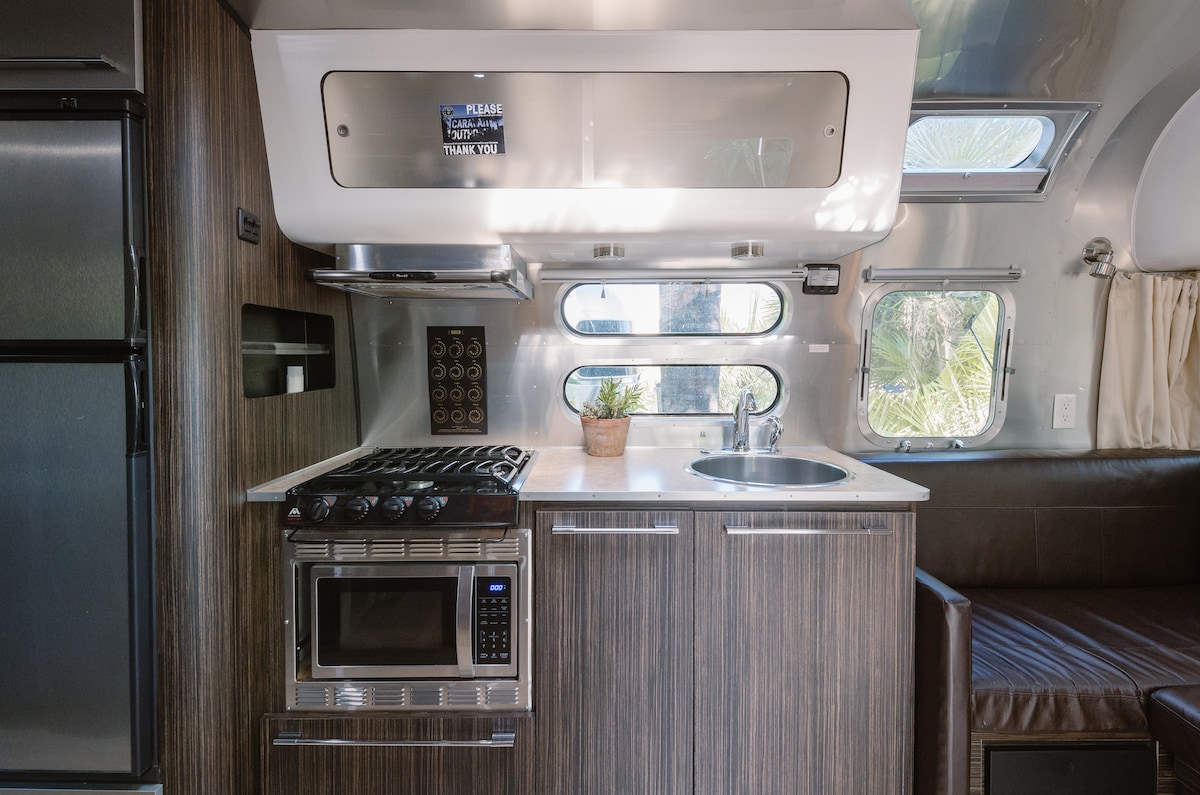 A modern kitchen area is featured, showcasing sleek cabinetry and a combination of appliances. A gas stove, microwave, and sink are included, with windows allowing natural light. A small potted plant adds a touch of greenery to the countertop.