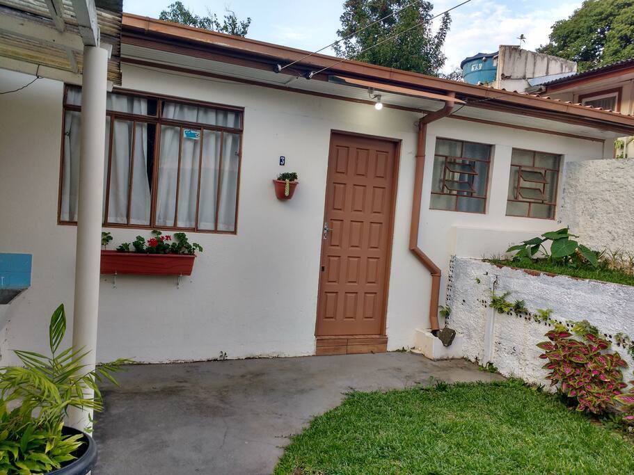 Visão da fachada da edícula, com jardim particular separado da restante da propriedade com muro e portão.