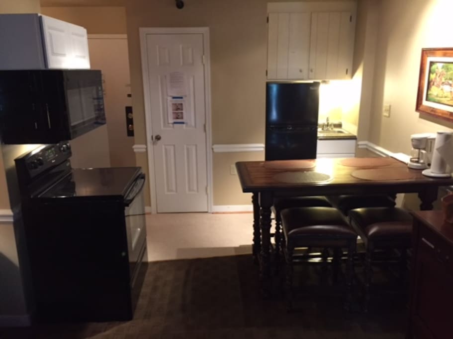 Small kitchen area includes a full-sized range and microwave, a 10 cubic foot fridge/freezer, a small sink, and many small appliances as well as posts, pans, utensils. and