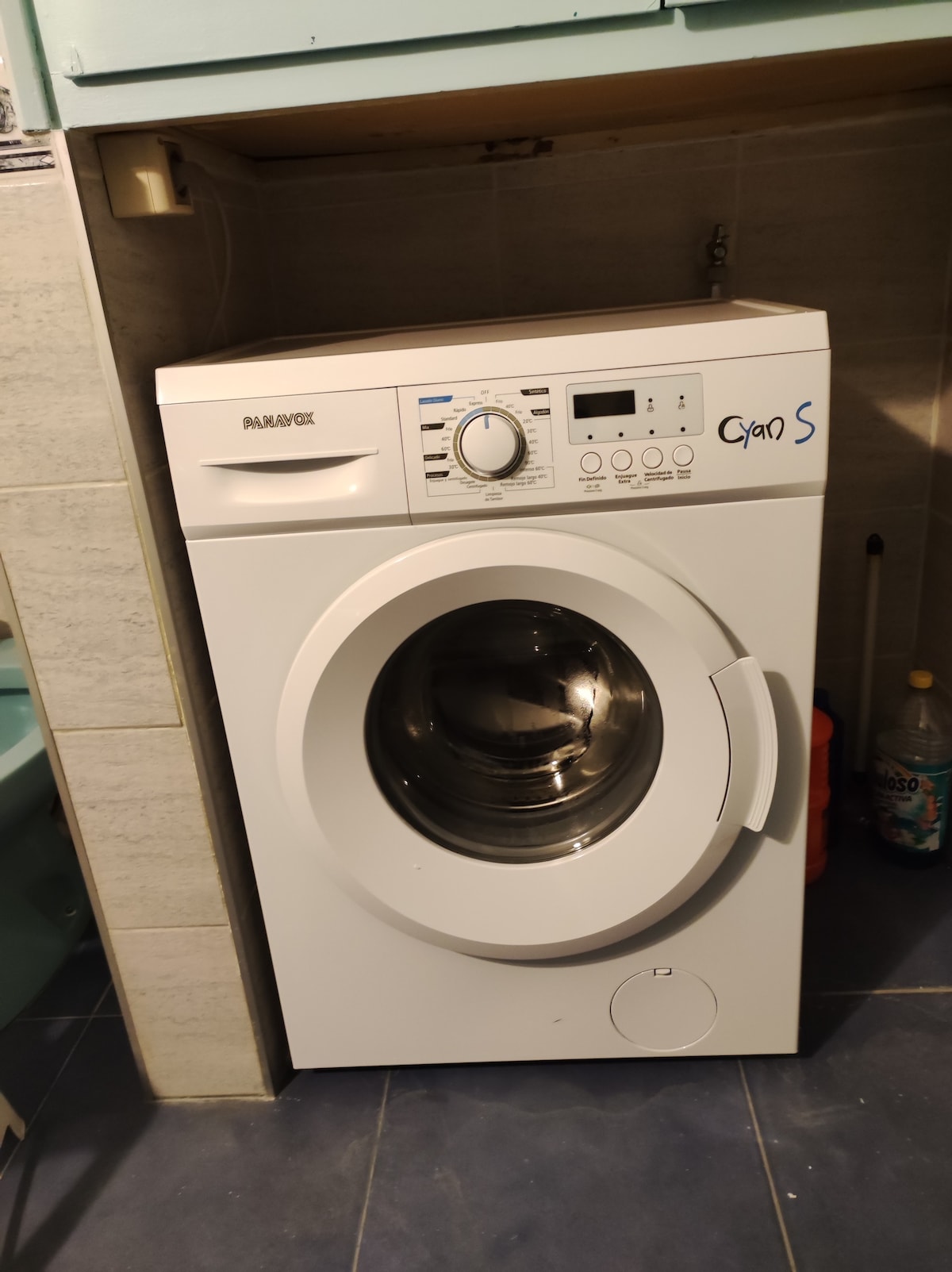 A front-loading washing machine is positioned against a tiled wall, featuring a circular glass door and a user-friendly control panel. It is designed for convenience, providing laundry capabilities within the listing.