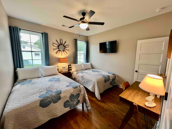 Third bedroom boasts two queen beds, nightstand with electric + USB charging ports, and wall-mounted 43 inch smart Roku TV.

