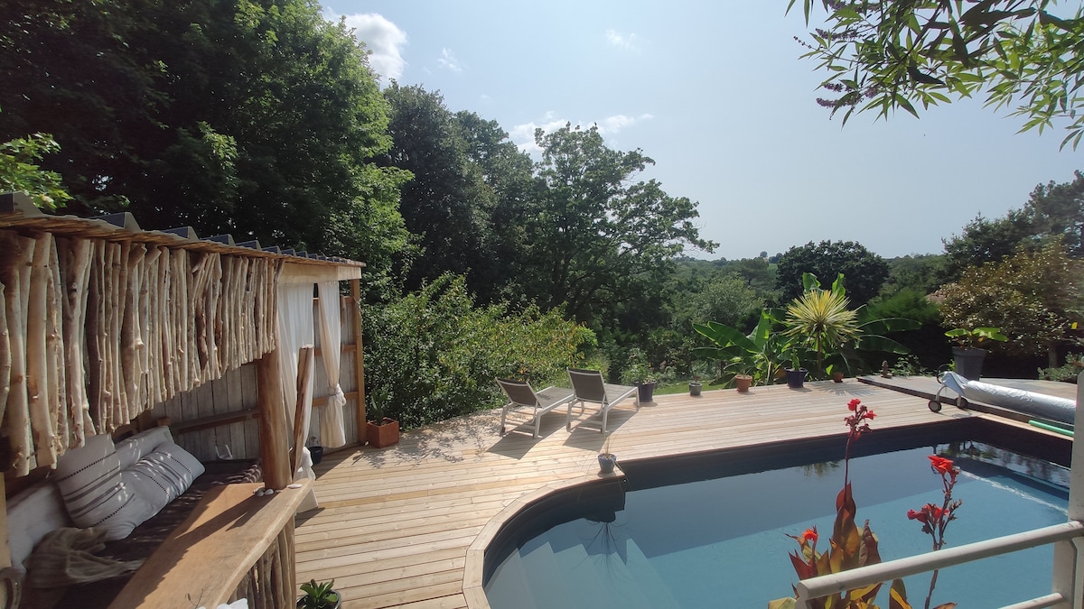 A wooden deck surrounds a heated pool, featuring lounge chairs positioned for relaxation. Lush greenery and trees create a natural backdrop, enhancing the tranquil atmosphere. Potted plants and vibrant flowers add touches of color to the space, inviting outdoor enjoyment.