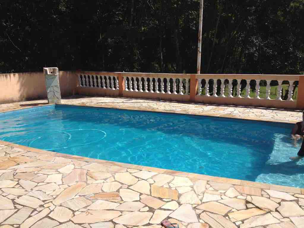 A private swimming pool is framed by a spacious stone patio. The clear blue water reflects sunlight, creating a relaxing atmosphere. Surrounding the pool is a decorative railing that offers views of the lush greenery beyond.