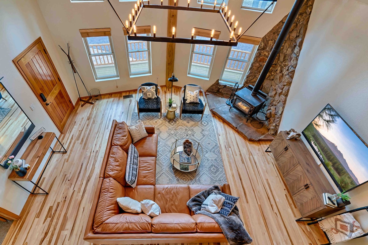 A spacious living area is captured from an elevated angle, featuring a large leather sectional sofa paired with two stylish armchairs. A coffee table sits centrally, complemented by a decorative rug. Large windows allow natural light to illuminate the room, where a modern fireplace provides warmth.