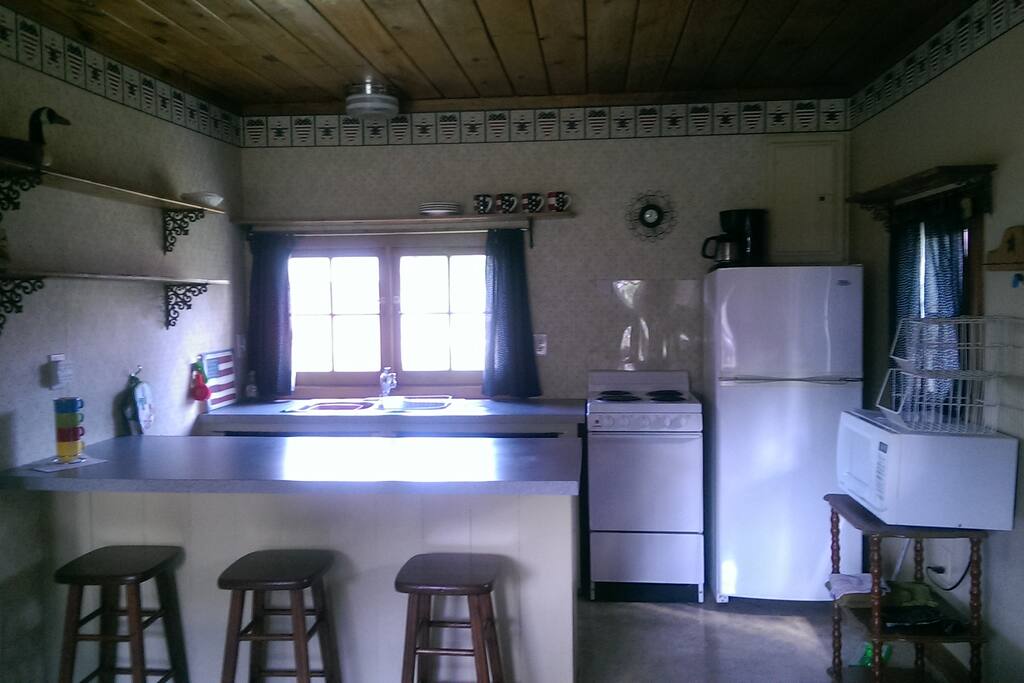 View of kitchenette. Includes stove, refrigerator, microwave, coffeemaker and dishes.