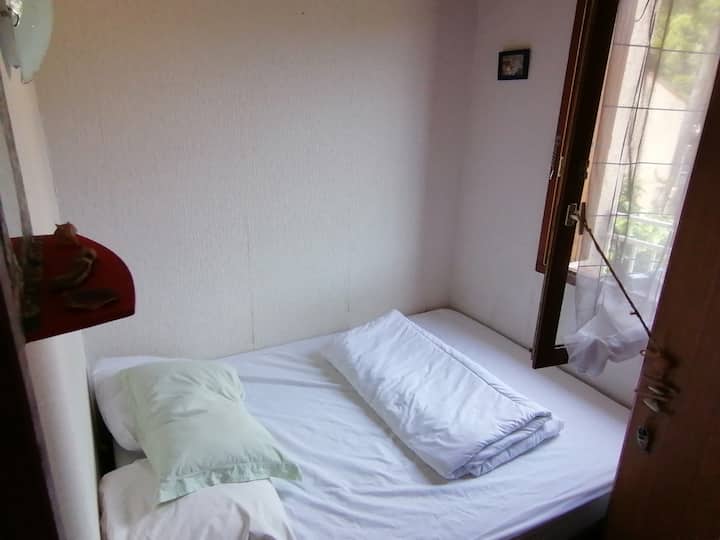 Stanza da letto piccola con 140 letti e piccolo armadio. Una colonna e un ventilatore rinfrescanti. 