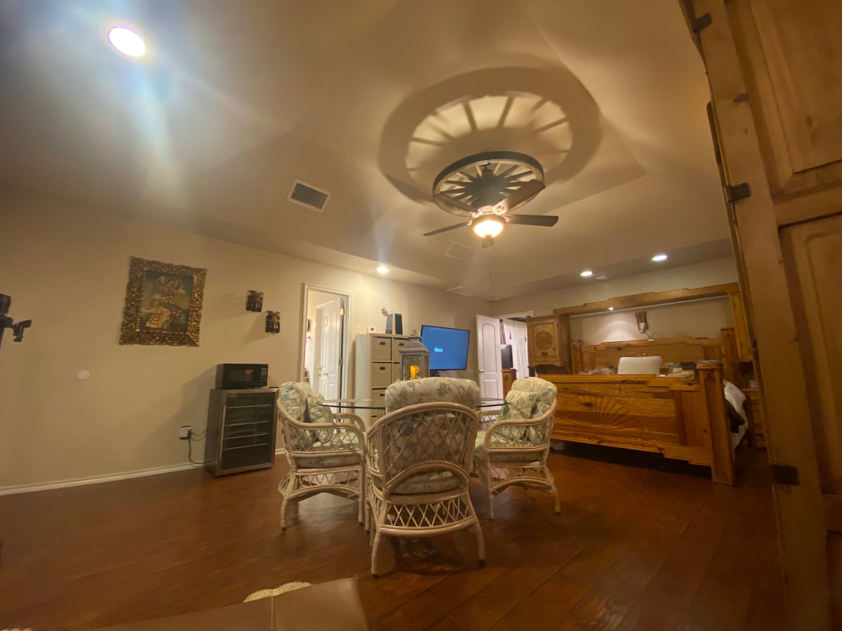 A spacious living area is furnished with wicker seating, featuring a TV positioned within a wooden cabinet. The adjustable king bed is visible in the background, with soft lighting illuminating the room. A microwave is noted on a side surface, enhancing convenience.