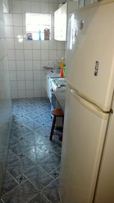 Cozinha com fogão 4 bocas, geladeira com freezer, e utensílios de cozinha, mais área de serviço com tanque e varal.