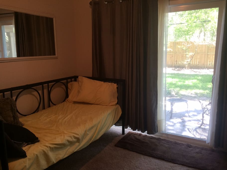 Guest room includes a twin bed, patio access, black out curtains, a desk, and window AC unit.