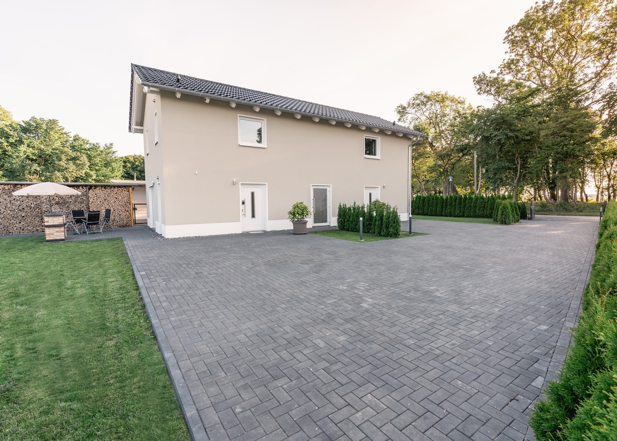 The exterior of the building is showcased, featuring a two-story structure with a light-colored facade. A spacious paved area surrounds the building, offering parking space. Lush greenery lines the property, providing a natural contrast to the paved surroundings.