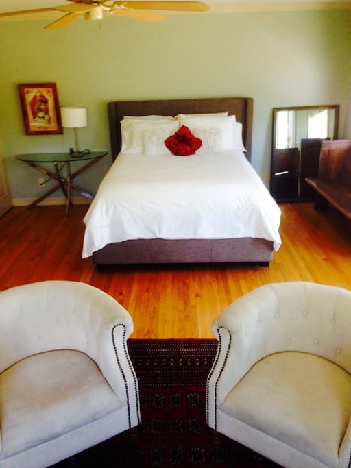 Large, bright, airy, ground floor master bedroom; glass doors open to garden. Room has hardwood floors and living space that includes couch, chairs, dressers and closet space.