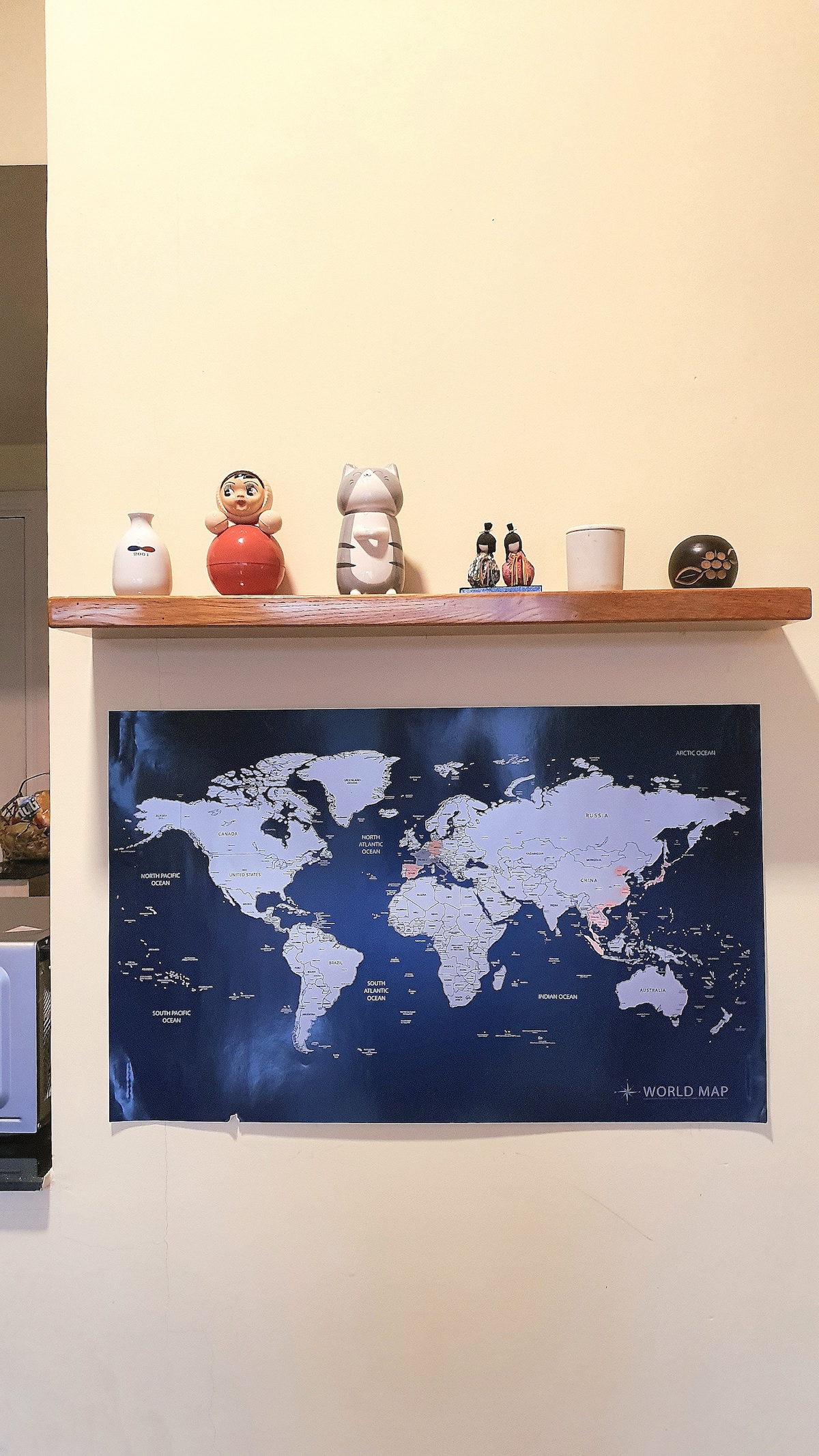 A wooden shelf displays decorative items, including figurines and a candle, above a world map. The map features geographical details in a contrasting color, serving as a focal point against the pale yellow wall.