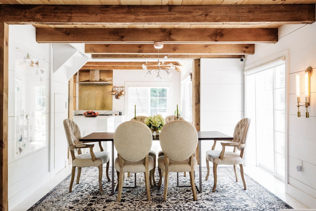 Dining Room With Reclaimed Wood Ceilings
Reclaimed wood beams continue into the dining room, where they infuse the space with warmth. Tufted armchairs complement the country aesthetic while still feeling sophisticated.