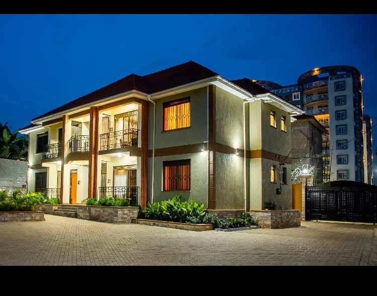 The exterior of the property features a two-story building with a well-lit facade. A spacious parking area is visible in the foreground, complemented by landscaped greenery. Modern architectural elements are present, and the surrounding environment is peaceful, indicating a quiet residential neighborhood.