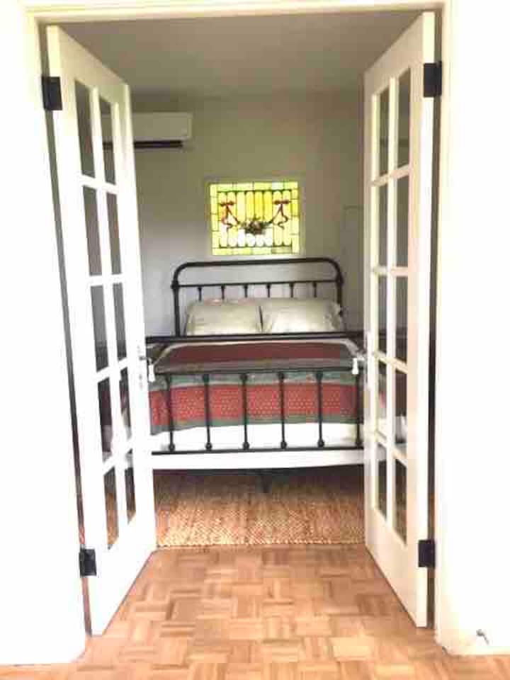 Dhoma e gjumit në katin e parë, me krevat dopio "queen" nën dritaren e xhamit me njolla.