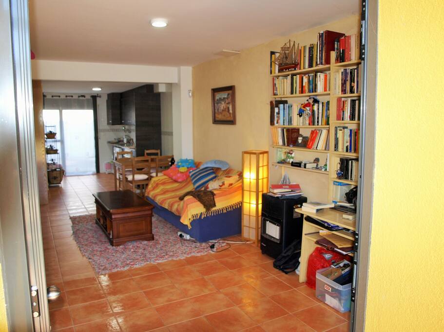 Os invitamos a compartir uno de los placeres de la casa: los libros. Al fondo, la cocina equipada.