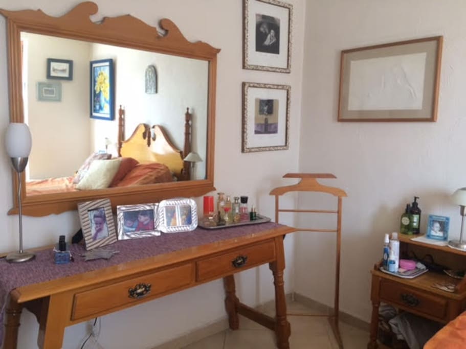 Un tocador con amplio espejo y un banco para tu maleta