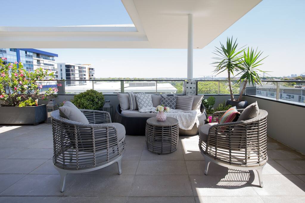 Rooftop lounge overlooking pools, gyms, historic architecture, with views of Sydney CBD and ANZAC bridge