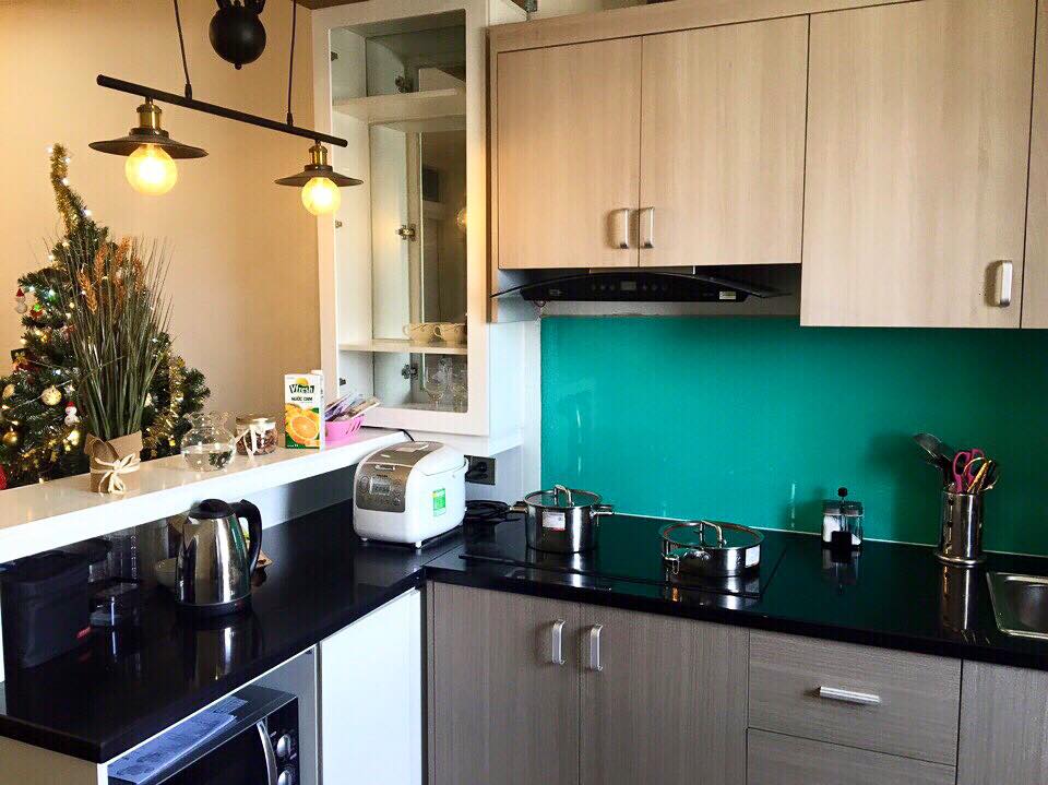 The kitchen showcases modern cabinetry with a sleek black countertop. A vibrant teal backsplash adds a pop of color. Essential appliances, including a kettle and a microwave, are neatly arranged, while pots and utensils are organized for convenience. Soft lighting contributes to a welcoming ambiance.