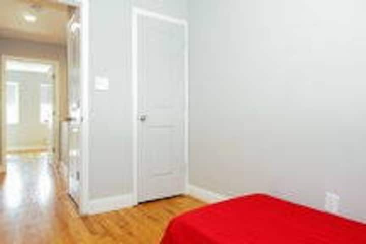 Позицијата на креветот е променета и собата сега вклучува бел дрвен гардеробер и мало бело дрвено биро