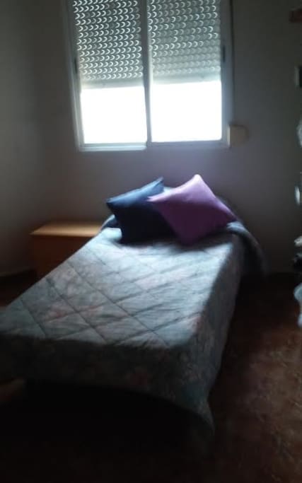 Habitación iluminada con armario, librero y mesita de noche con cajones.