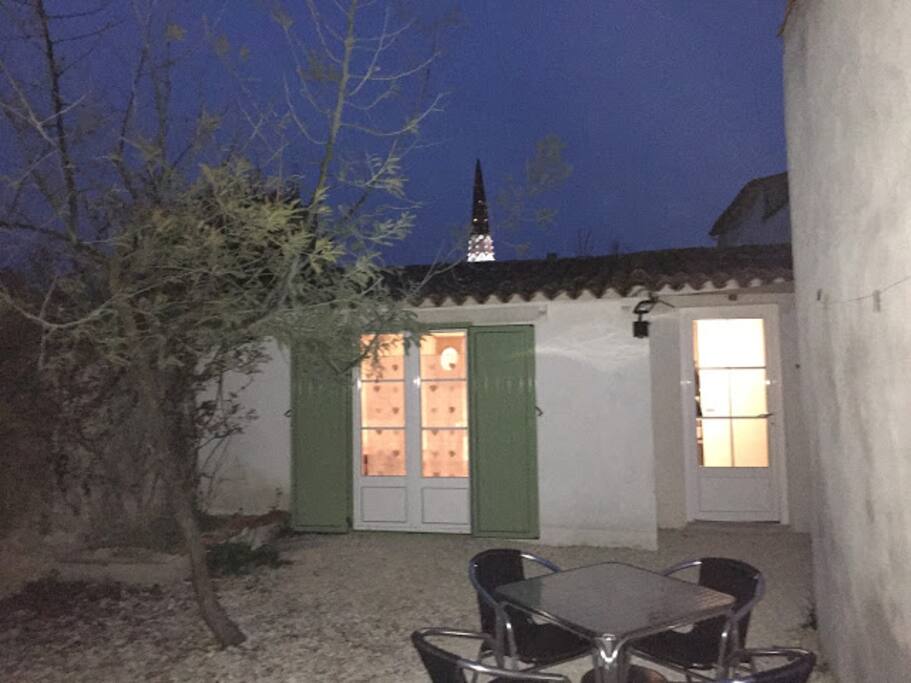 Vue sur le clocher d'Ars, table de repas devant la chambre, parasol, transat.