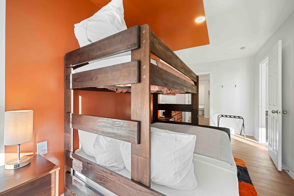 - חדר שינה נעים עם מיטת קומותיים, קיר עיצובי בצבע כתום מודגש ותאורה חמה - מיטות קומותיים עם מסגרת עץ יציבה, מושלמות למשפחות או לקבוצות - נכס Airbnb מהנה ומזמין, שעוצב מתוך מחשבה על נוחות  