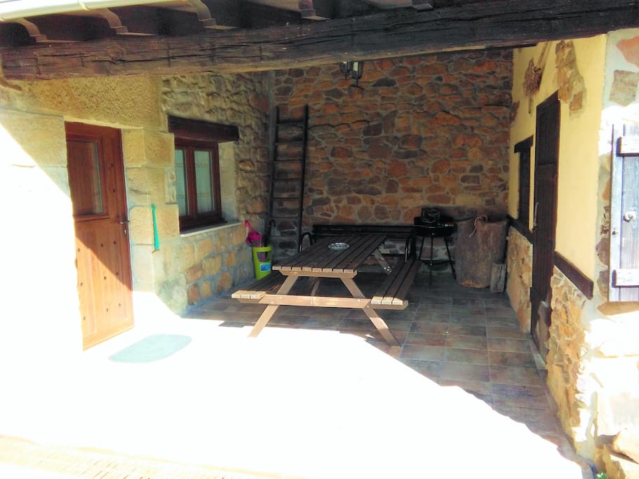 Porche de la casita con disponibilidad de barbacoa y mesa con sillas de jardín.