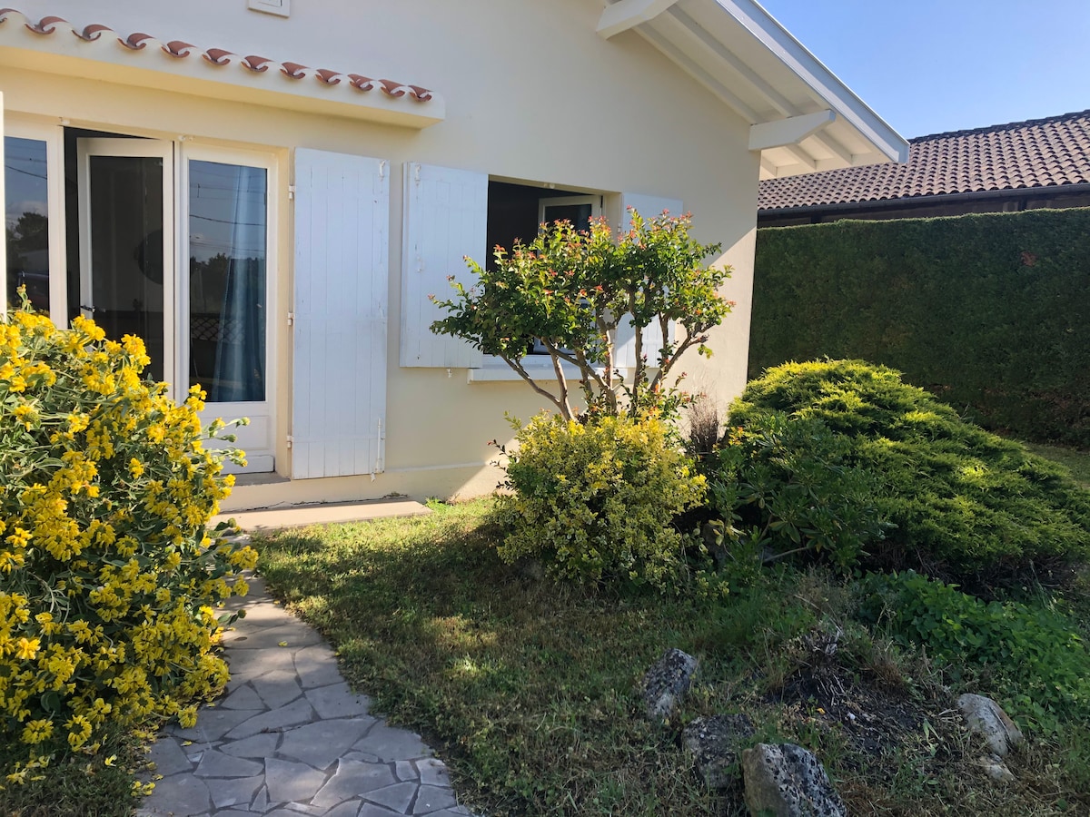The exterior of a charming independent house is framed by vibrant greenery and blooming yellow flowers. A stone pathway leads to the entrance, where white shutters enhance the fresh look of the exterior. Lush shrubs create a tranquil garden setting.