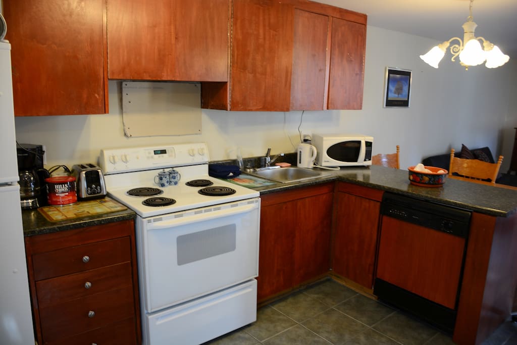 Roomy kitchen with lots of dishes, dishwasher, small appliances of microwave, coffee maker, toaster and kettle