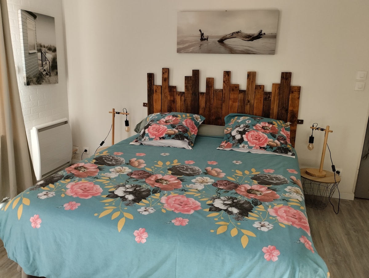 A bed is presented with a floral-patterned duvet cover featuring soft shades of blue, pink, and green. Wooden headboard adds a rustic touch. Two bedside lamps provide gentle lighting, and a black-and-white photograph hangs on the wall above the bed.