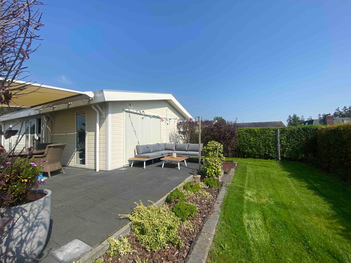 A spacious outdoor area is presented, featuring a cozy lounge set with cushions and a well-maintained garden. The inviting patio is complemented by a sun awning, and the surrounding greenery adds privacy to the location.