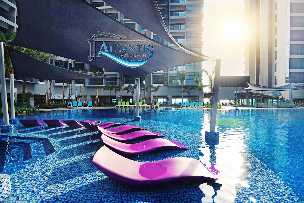 A well-designed swimming pool area is highlighted by vibrant purple lounge chairs arranged alongside the water. Sunlight reflects off the pool's surface, creating a serene atmosphere. Shade structures provide comfort, while the surrounding greenery enhances the setting's tranquility.