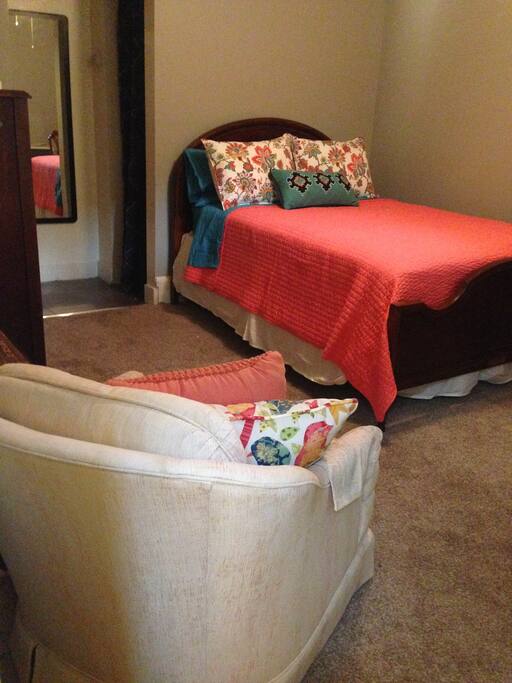 Cozy bed/sitting room with desk, reading chair, dresser, closet and double bed.