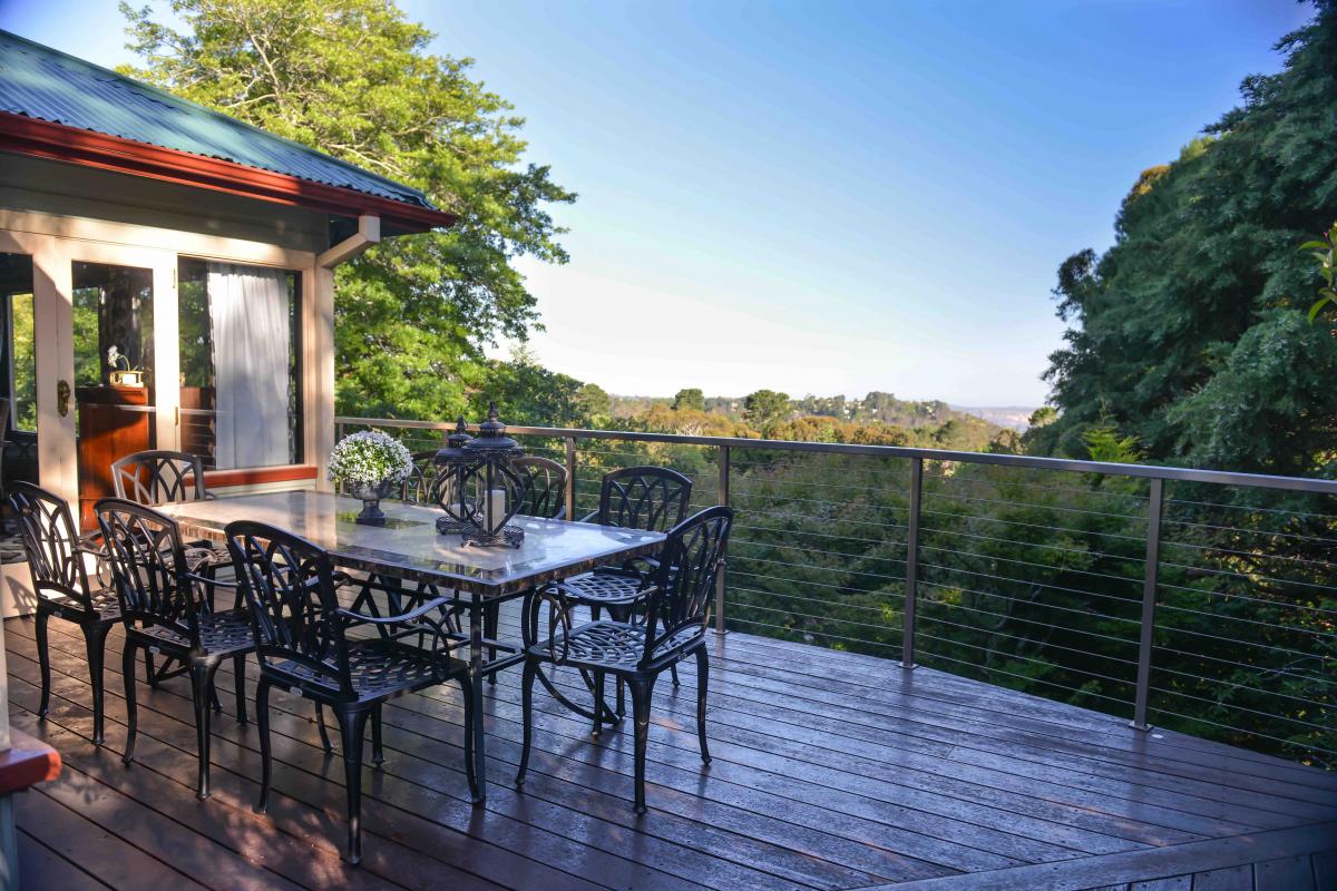 A spacious outdoor deck showcases a large dining table surrounded by elegant black chairs. Lush greenery frames the view, creating a serene backdrop. The area offers ample sunlight and a calm ambiance, perfect for gatherings while enjoying the natural surroundings.