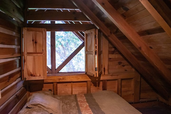 Втора спална соба, втор двоен кревет на прозорецот од внатрешноста на дрвената колиба 